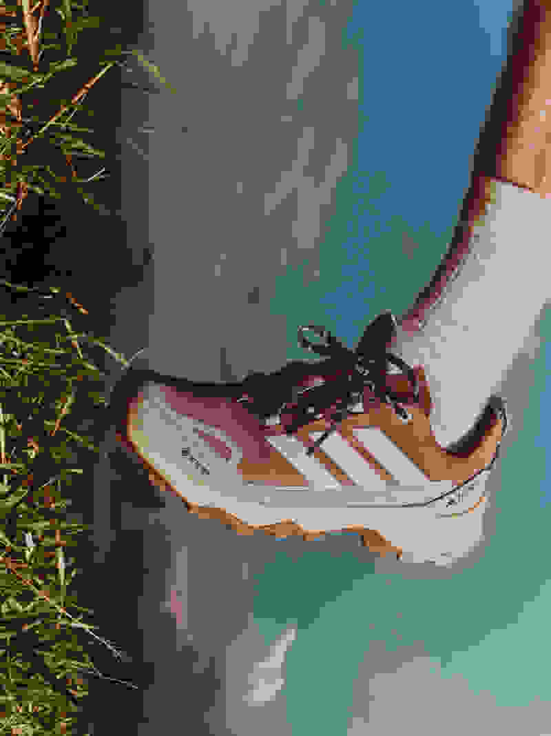 En vandresko med en robust sål hviler på en græsdækket overflade med en skyet blå himmel synlig i baggrunden.