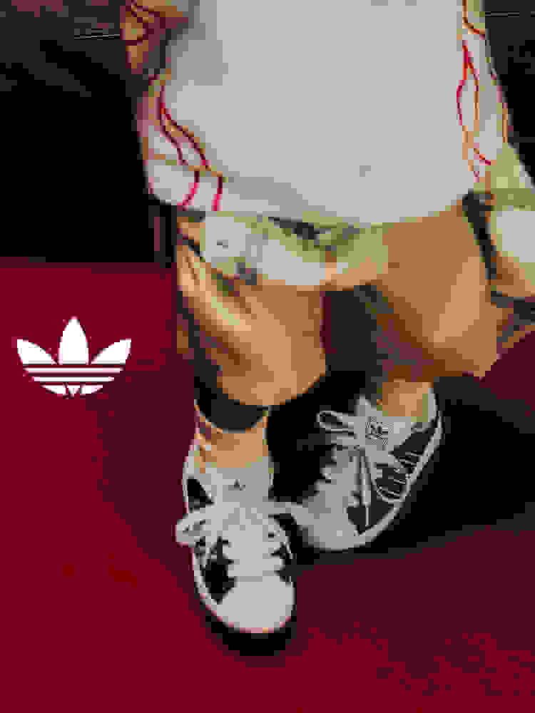 Close-up of a child wearing black-and-white adidas Superstar kids' sneakers on a red carpet, with the Trefoil logo overlayed on the left.