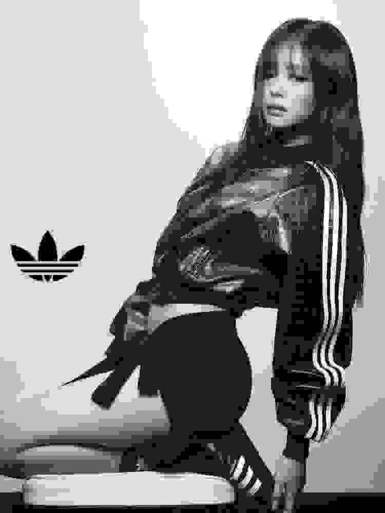 JENNIE sits on a chair wearing a textured adidas jacket with three-stripe sleeves and shorts and black adidas Superstar trainers, next to the Trefoil logo.
