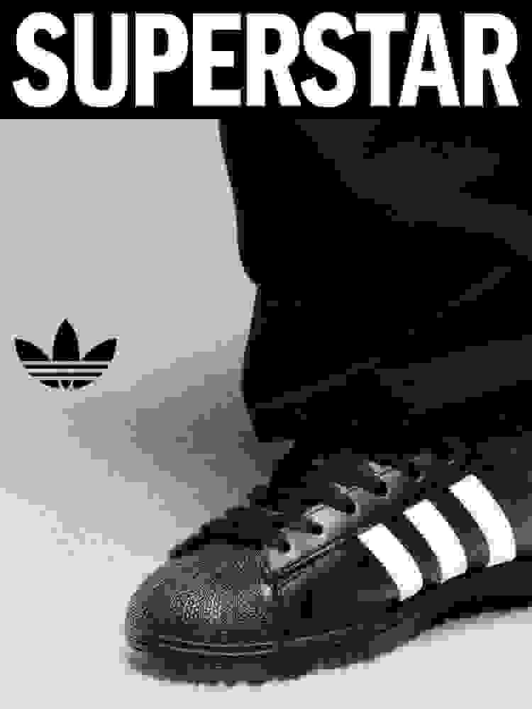 Black and white image of a person's legs wearing black adidas socks and black adidas Superstar trainers with white stripes. The word "SUPERSTAR" is in bold white text at the top, and the Trefoil logo appears to the left of the legs.