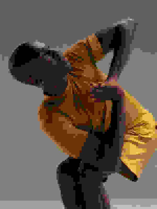 A person in a yellow shirt is captured in a dynamic, expressive pose against a neutral background.