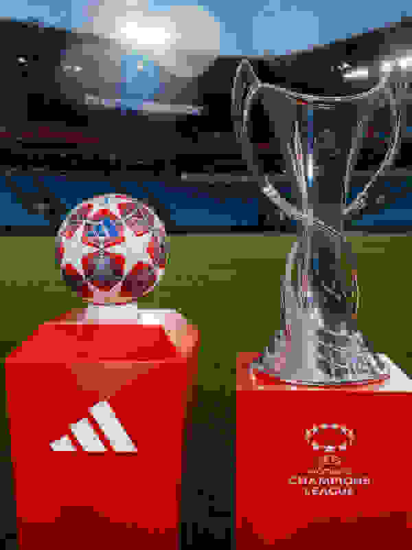 The image shows a large trophy and a soccer ball on a red pedestal in the foreground, with a soccer stadium in the background.