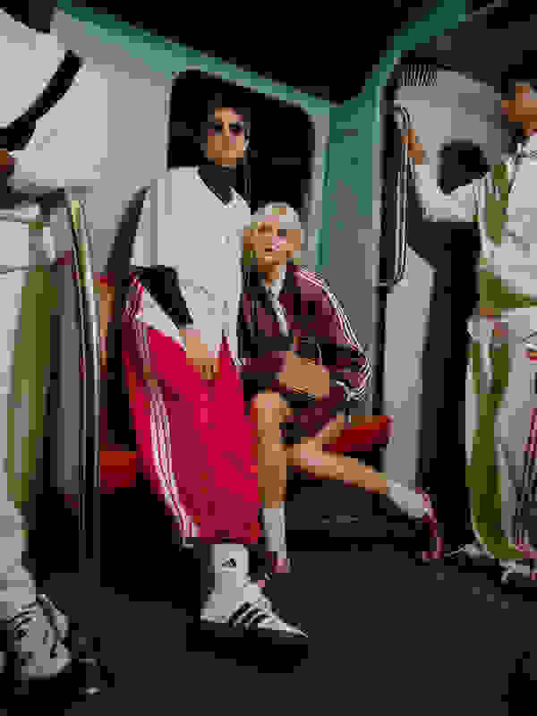 The image depicts two individuals, a person wearing a white jacket and a person wearing a red jacket, sitting in what appears to be the interior of a vehicle or transportation mode.