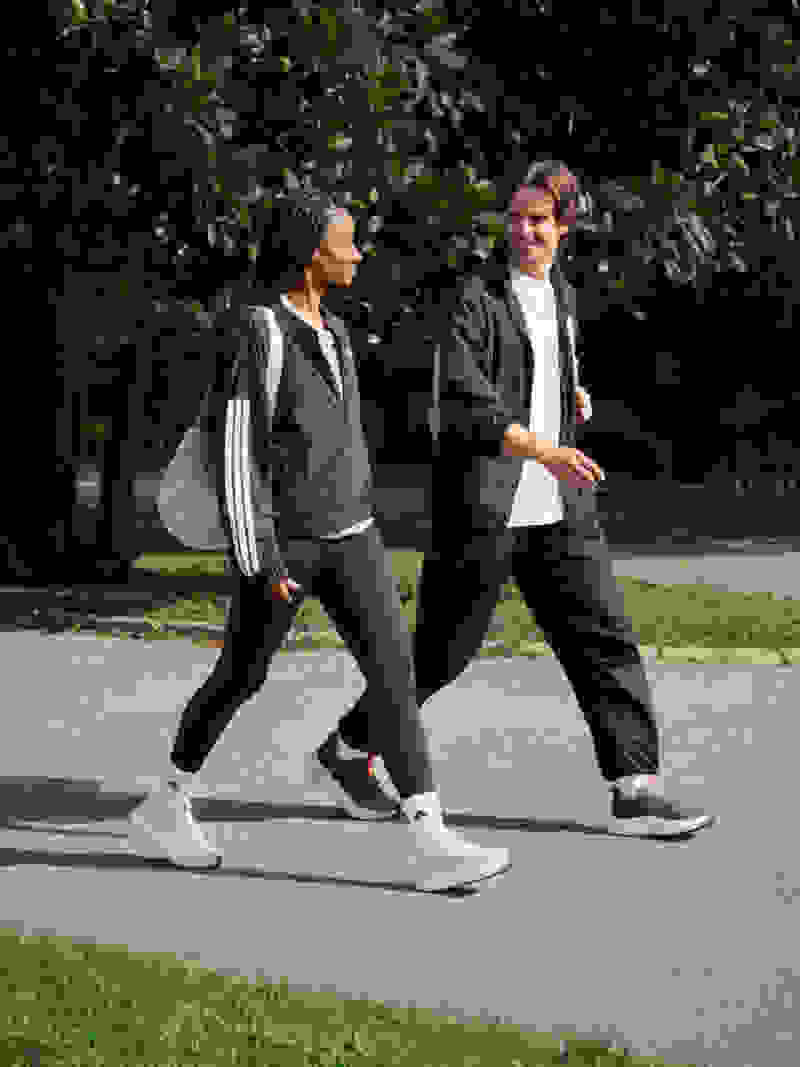 Two people, a woman and a man, are walking together on a paved path in a park surrounded by lush greenery.