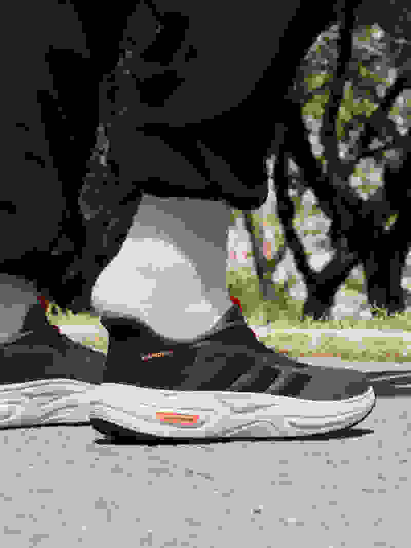 The image shows a pair of black and gray athletic shoes with white socks, set against a background of trees and foliage.