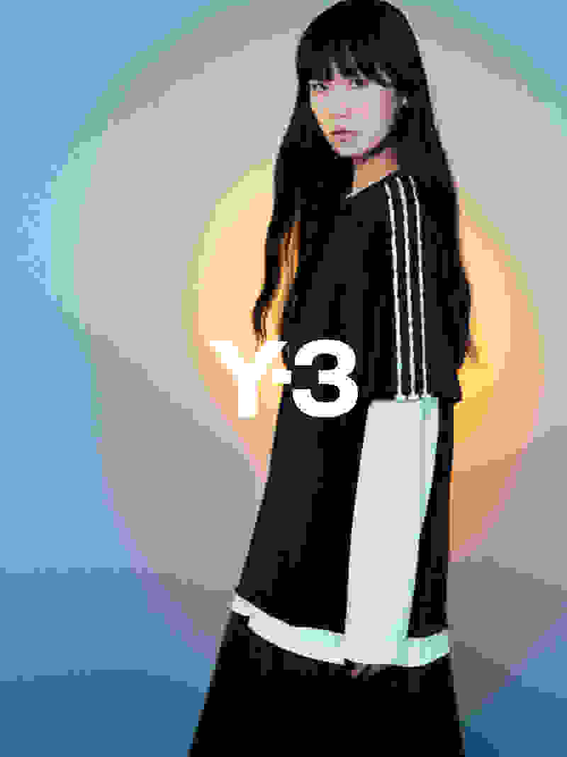 흑백 원피스를 입고 긴 검은 머리카락을 가진 젊은 여성이 일반 파란색 배경에 서 있다.