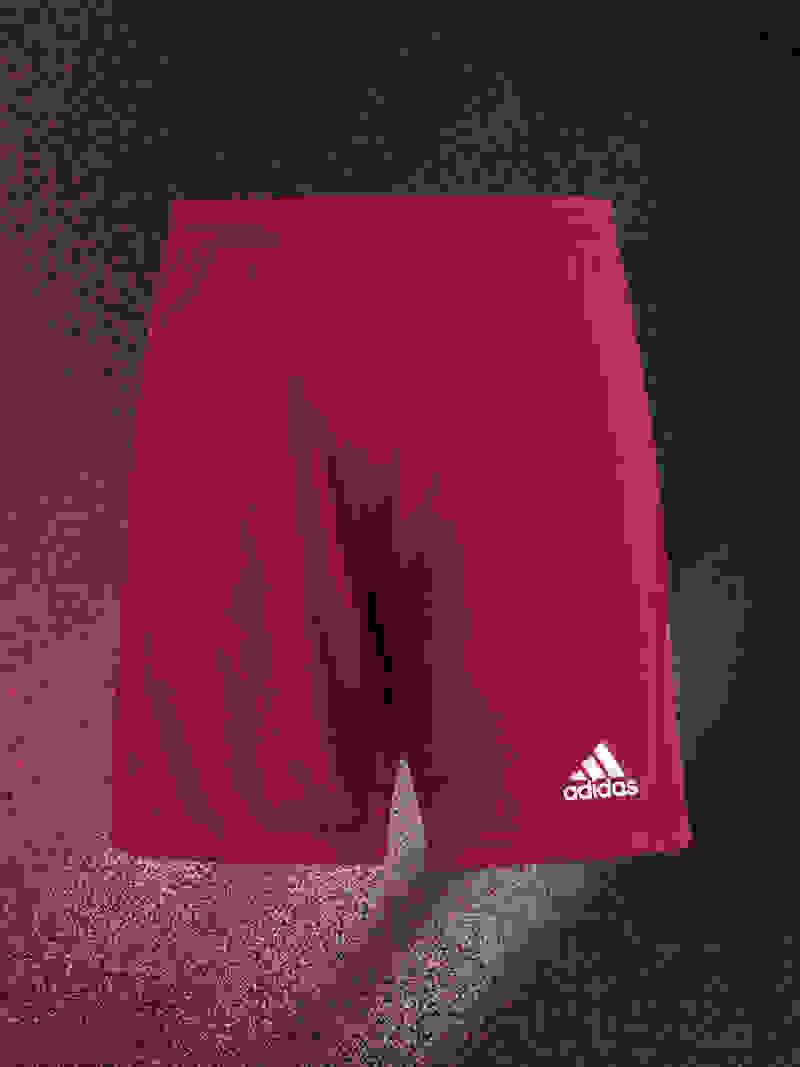 A pair of red Adidas athletic shorts against a dark, textured background.