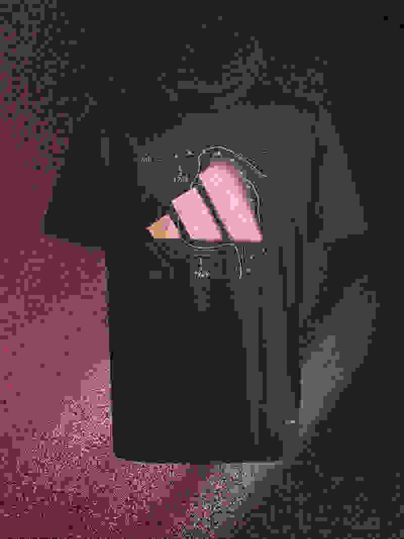A black t-shirt with a pink fish-like creature design printed on it, set against a dark, textured background.