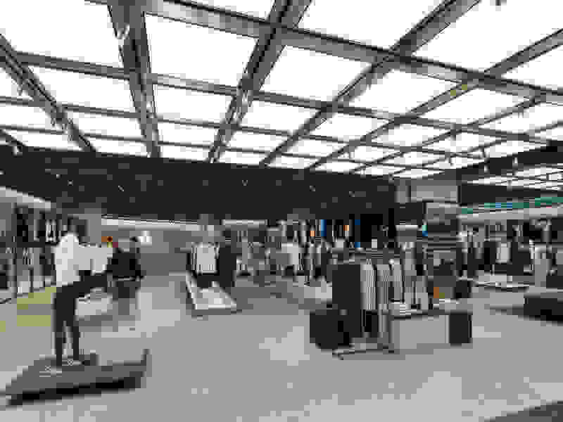 A modern, well-lit clothing store interior with various apparel displays, mannequins, and a glass ceiling structure overhead.