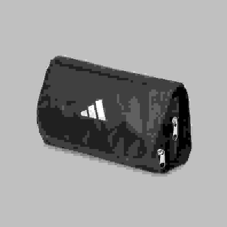 A black Adidas toiletry bag with the Adidas logo prominently displayed on the front, set against a plain gray background.