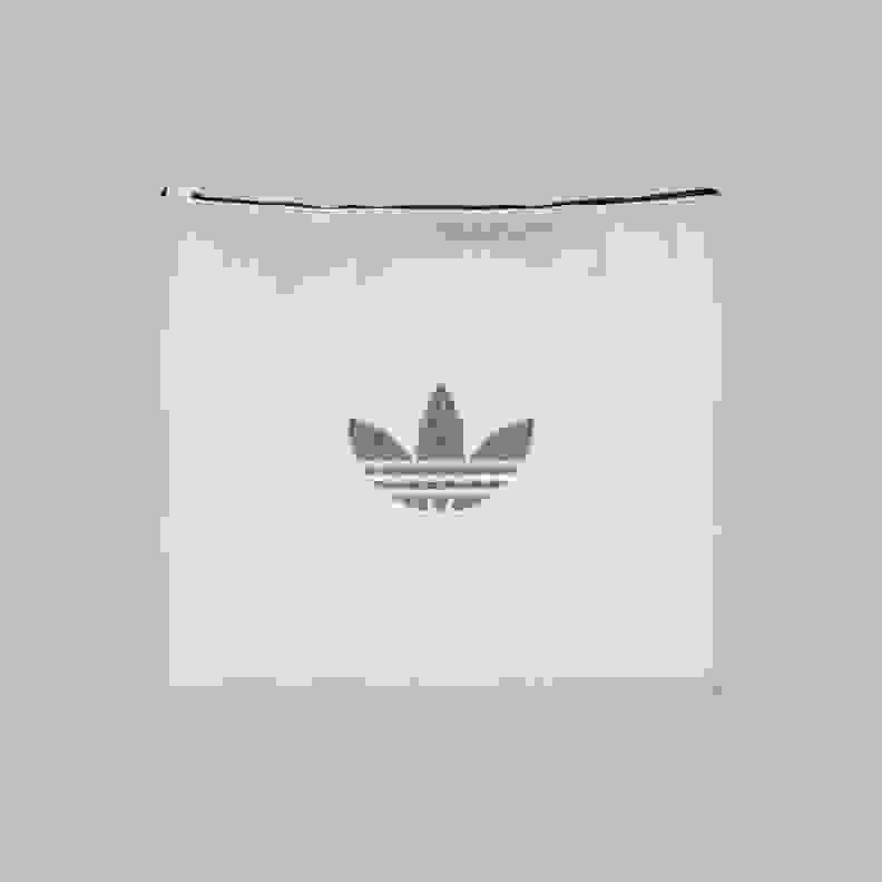 A white fabric pouch or bag with the iconic Adidas trefoil logo prominently displayed in a muted gray color against a plain background.