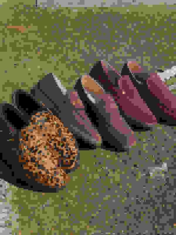 A collection of various loafer-style shoes, including a pair with a leopard print pattern, arranged on a gravel or pebble-covered surface.