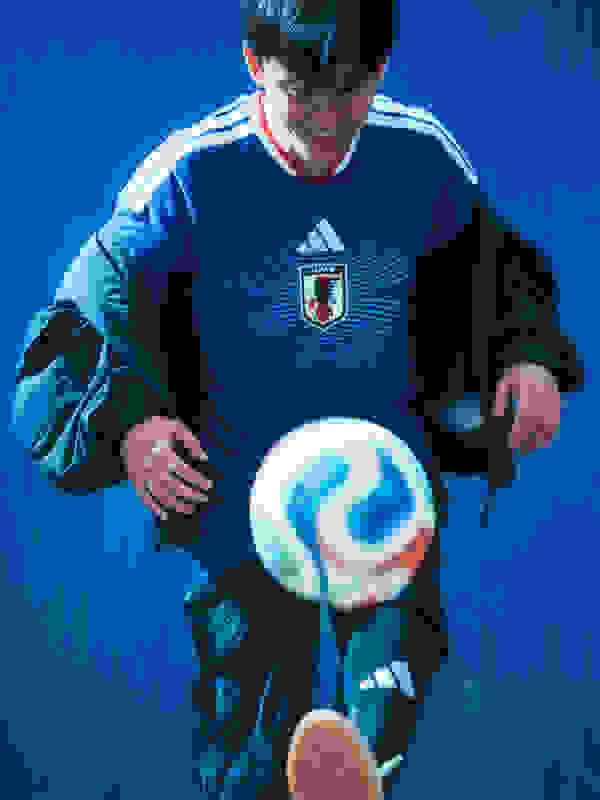 A young man in a blue and white soccer jersey is holding a soccer ball in front of a vibrant blue background.