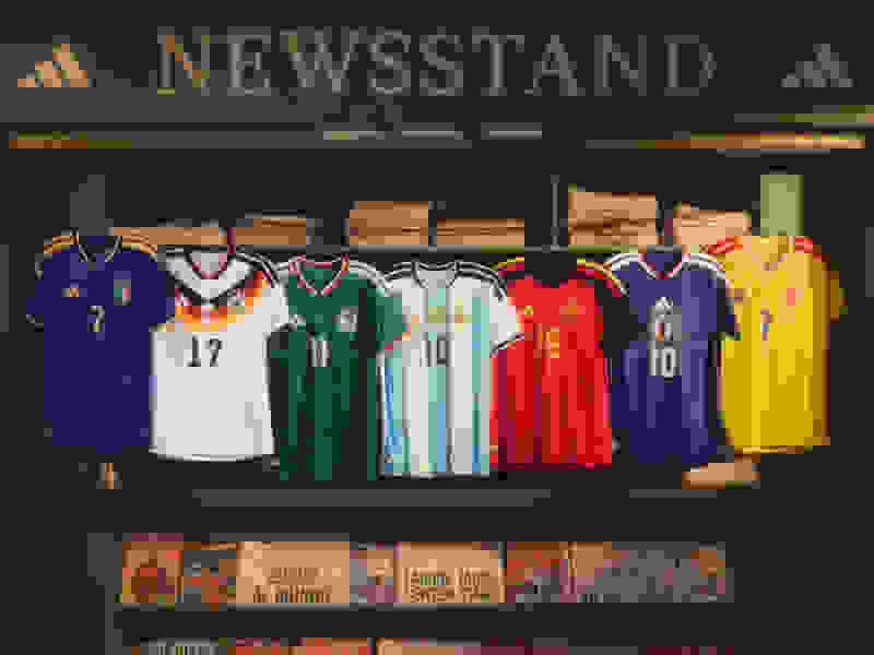 A newsstand display showcasing various national soccer team jerseys, with magazines and newspapers visible in the background.