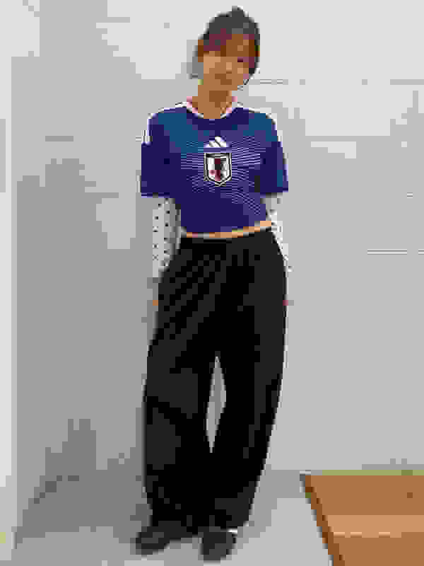 A young woman wearing a blue and white striped jersey and black pants stands in a room with white tiled walls.