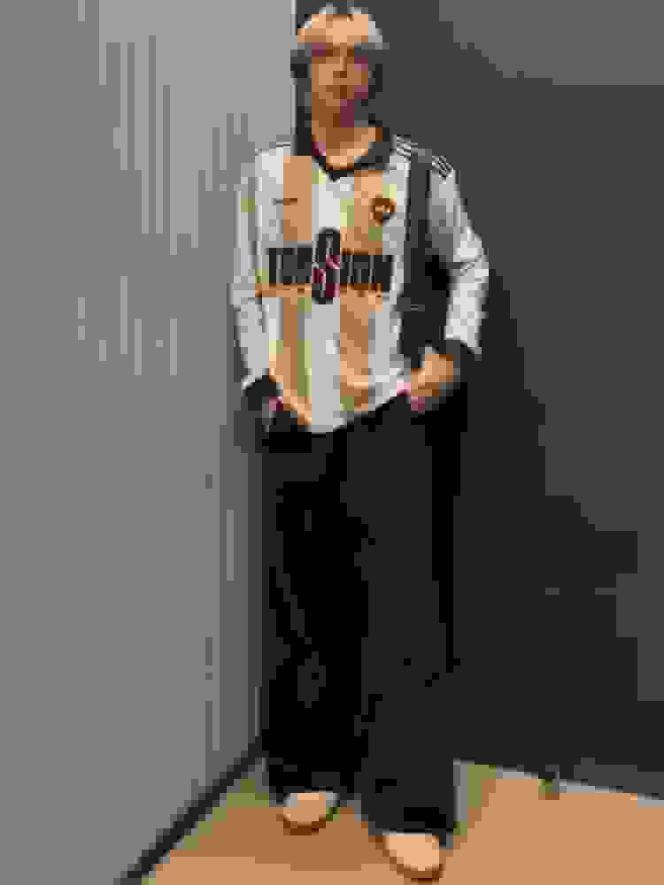 A person wearing a white and black sports jersey and black pants is standing in a hallway with a gray striped wall.
