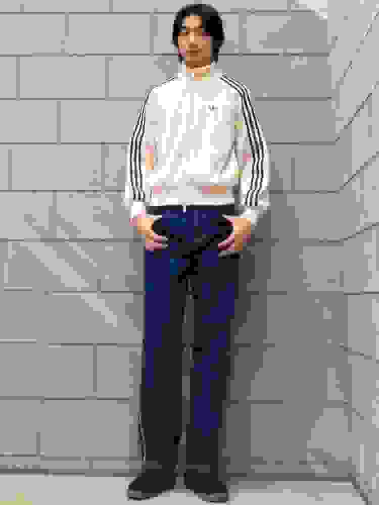 A young person wearing a beige jacket with stripes and standing in front of a gray brick wall.