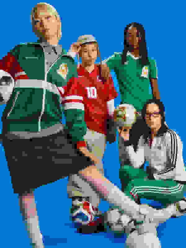 A group of diverse individuals, including a young boy wearing a red jersey, a woman in a green tracksuit, and a man with dreadlocks, are posing together with soccer balls and equipment against a vibrant blue background.