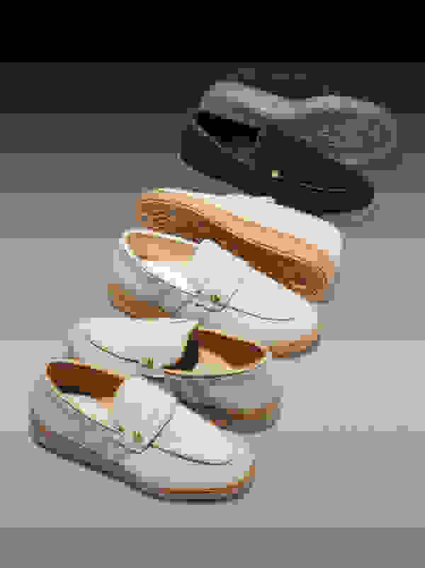 A collection of various casual loafer-style shoes in different colors, including navy blue, beige, and white, with contrasting soles and details.