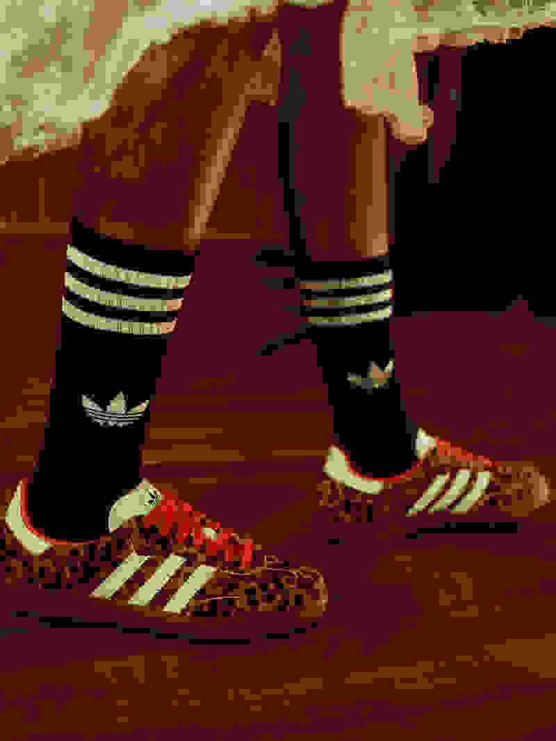 The image shows a pair of legs wearing black and white striped socks and leopard print sneakers, standing on a wooden floor.