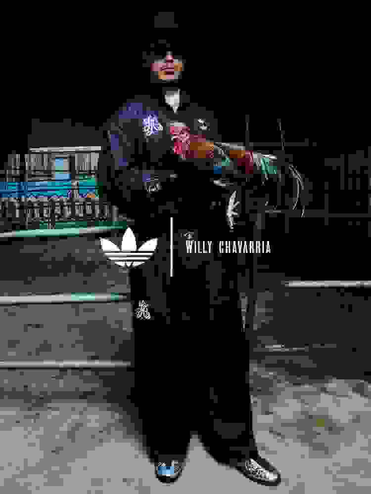 Närbild av en kvinna som bär en blå tröja från adidas x Willy Chavarria i "Los Angeles" med en stor stjärngrafik och Trefoil-logga framtill. Hon står med armen vilande på axeln av en person som bär en svart "Chicano"-tröja från adidas Originals x Willy Chavarria.