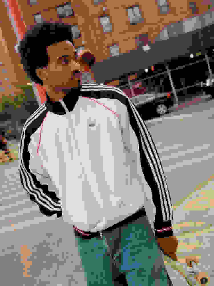 Tyshawn Jones sits on step, looking to camera, wearing white and brown adidas top and jeans