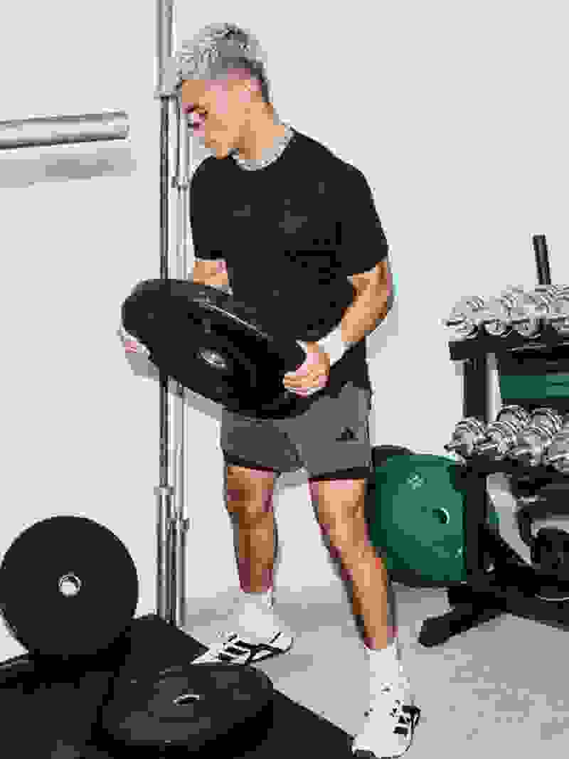 A person in athletic clothing is lifting weights in a gym setting, surrounded by various exercise equipment and weights.