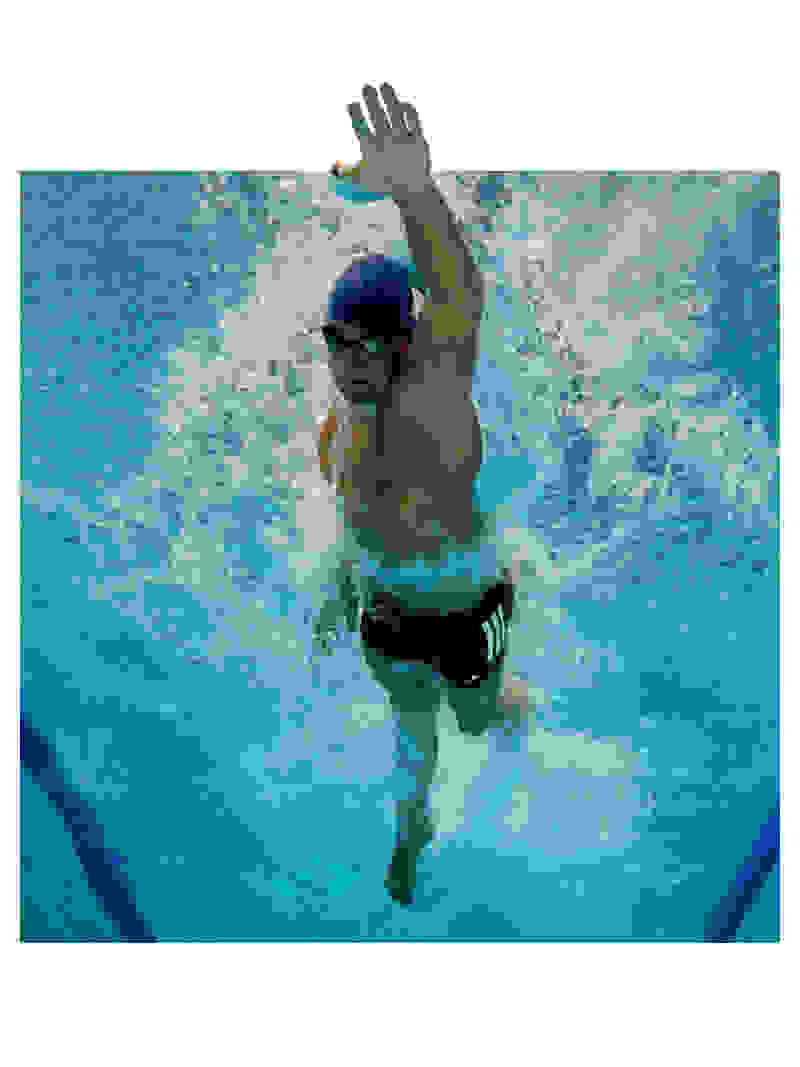 A person wearing a swim cap and goggles is swimming underwater in a pool, with water splashing around them.