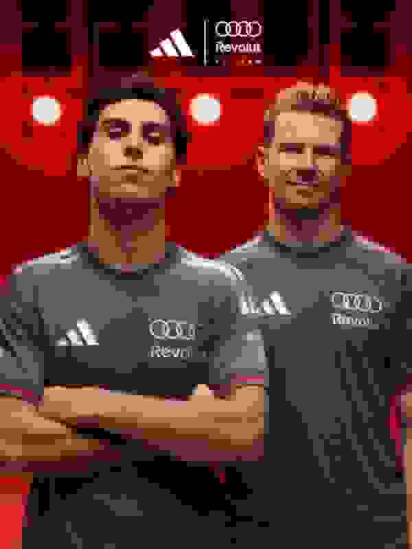 Two individuals wearing gray Audi Revolut jerseys stand in front of a red background with the Audi and Revolut logos prominently displayed.