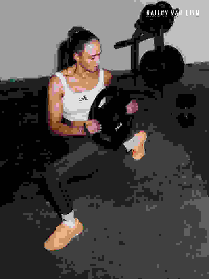 A woman in athletic wear is lifting weights on a concrete surface, with a piece of exercise equipment visible in the background.