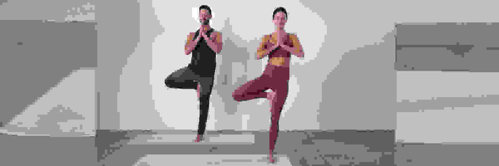 Zwei Frauen in Sportkleidung führen Yoga-Posen vor einem weißen Hintergrund durch.