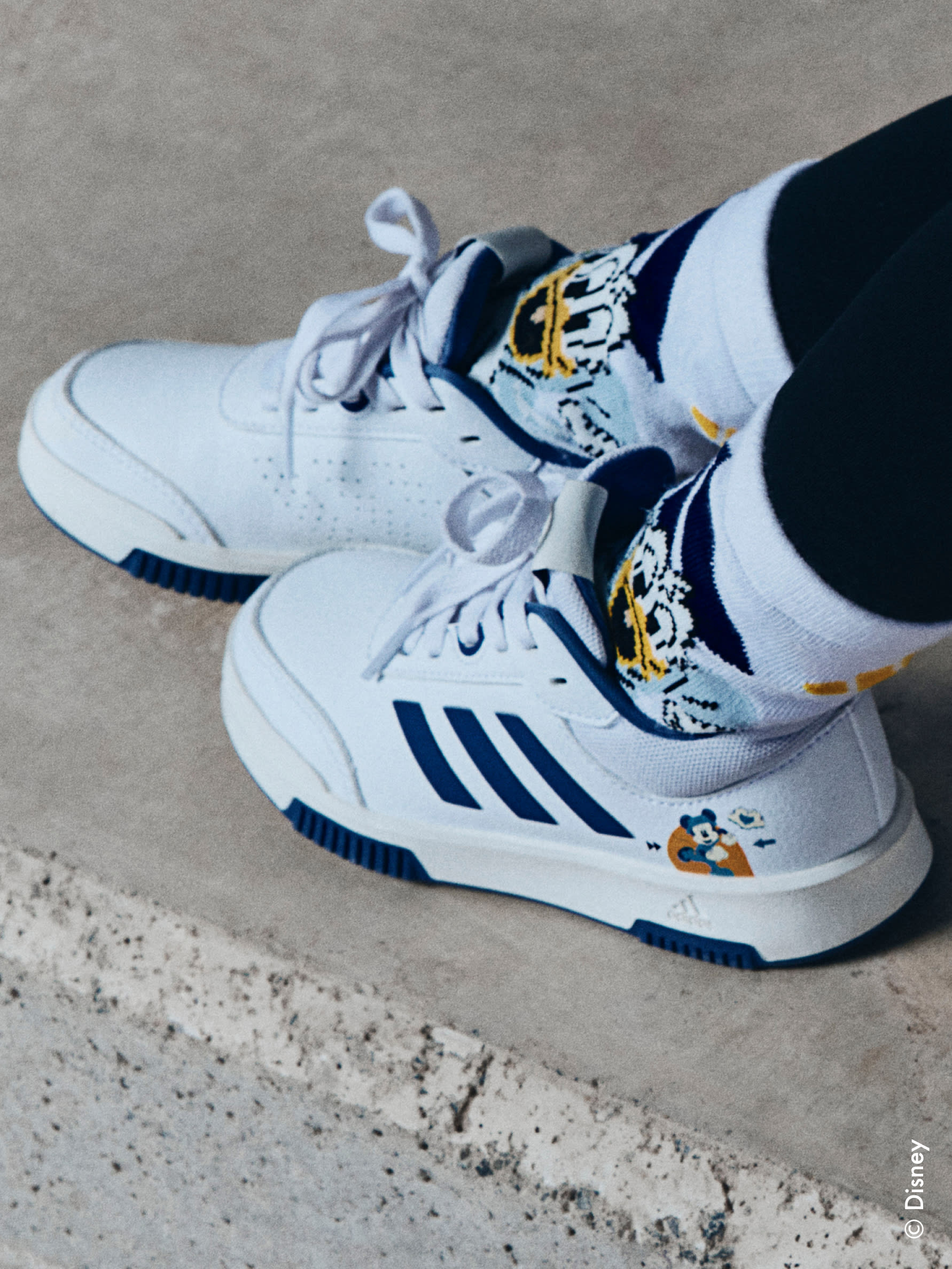One child standing on the street against a blue backdrop, wearing the adidas | Mickey & Friends collection.