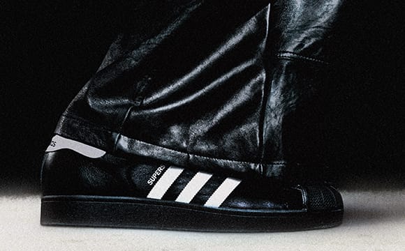 A close-up view of a person's foot wearing a black leather boot with the iconic three-stripe design of the Adidas brand prominently displayed.