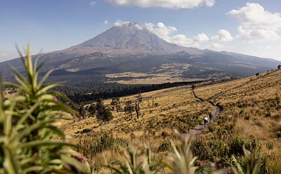 A volcano in the desert with two people cycling in the foreground