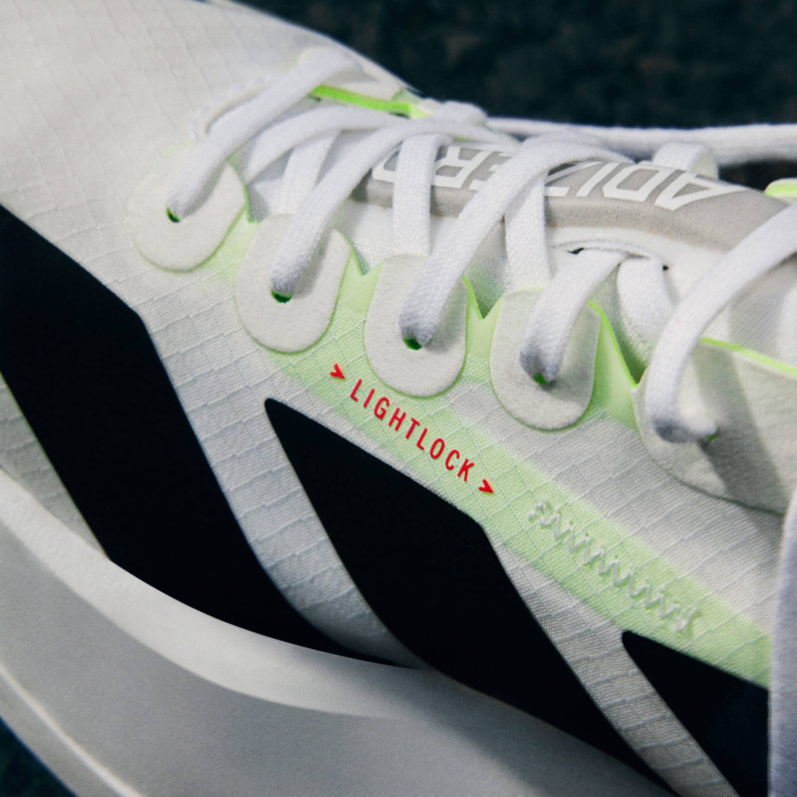 The image shows a close-up view of a pair of white sneakers with green accents, featuring a "Lightlock" label on the side.
