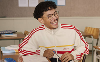 Image of teenage boy sitting in a classroom wearing adidas apparel.