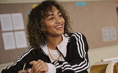 Image of a teenage girl sitting in a classroom wearing adidas apparel.