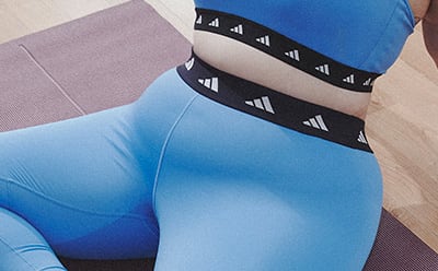 image of plus size model sitting in a stretching pose wearing a light blue sports bra and leggings co-ord with black trim