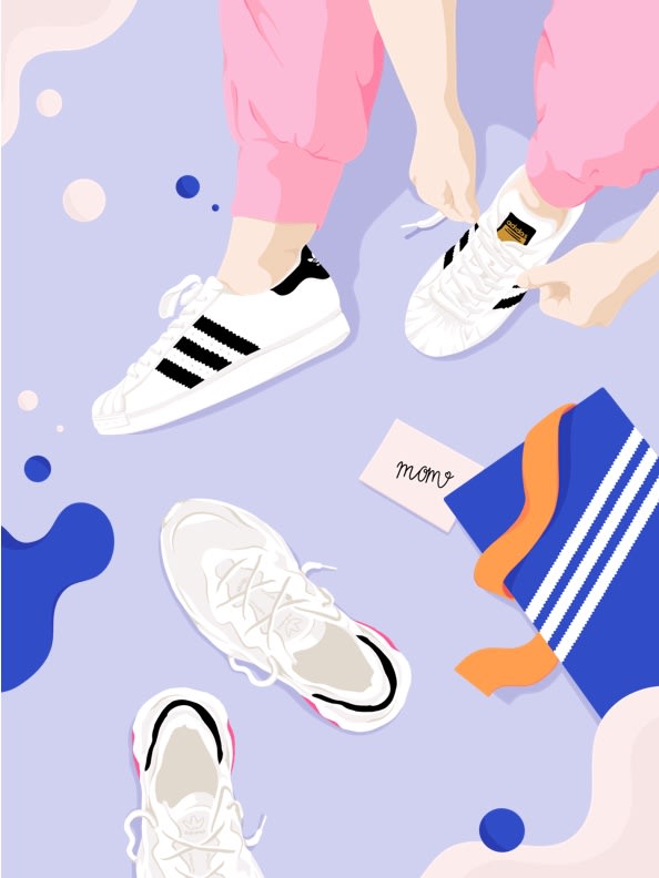 Top view of a moms feet as she puts on a new pair of Superstar shoes beside an open shoe box and a pair of UB21 sneakers.