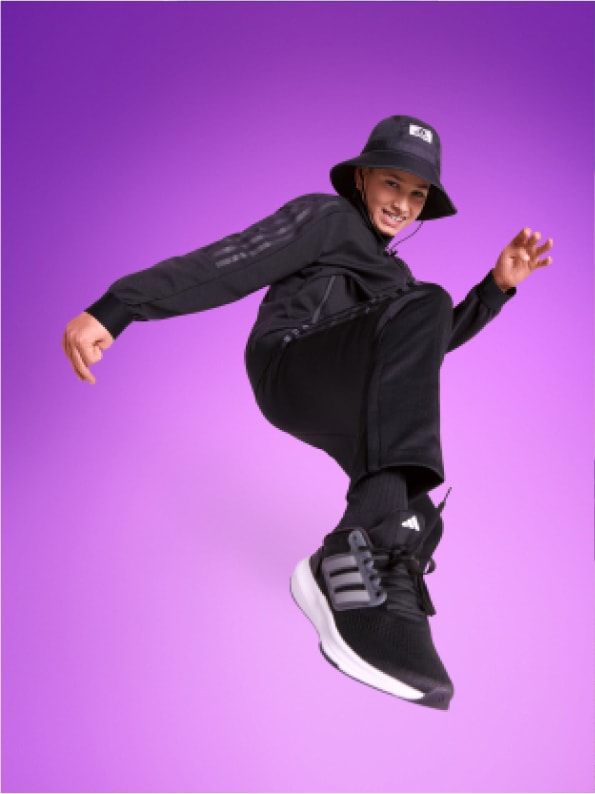 Smiling young boy posed mid-stride, dressed in adidas tracksuit and bucket hat.