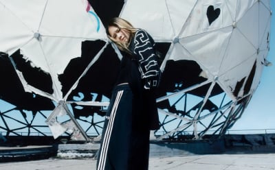 A woman with blonde hair stands in front of a graffiti wall in an industrial neighborhood while wearing Y-3 apparel.