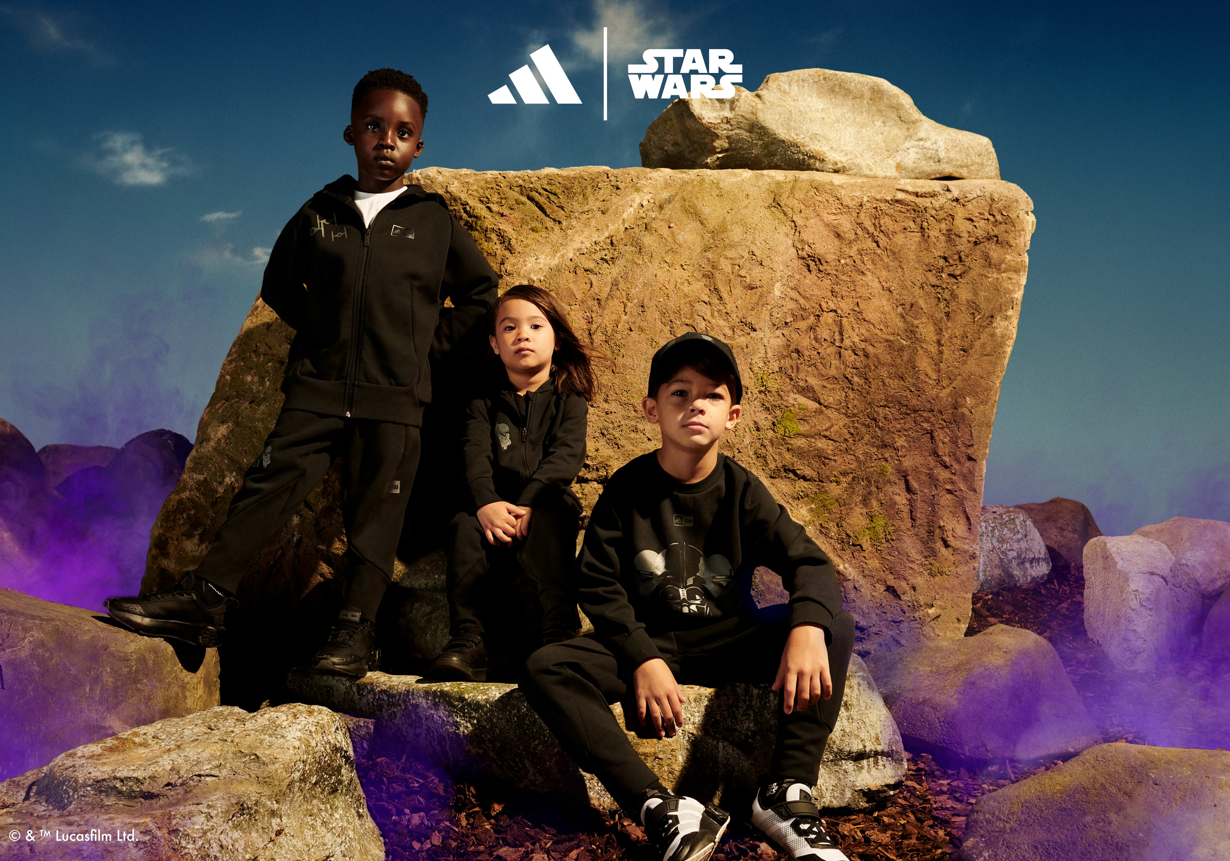 One child standing and two children sitting in font of rock with purple mist all wearing the adidas | Star Wars collection