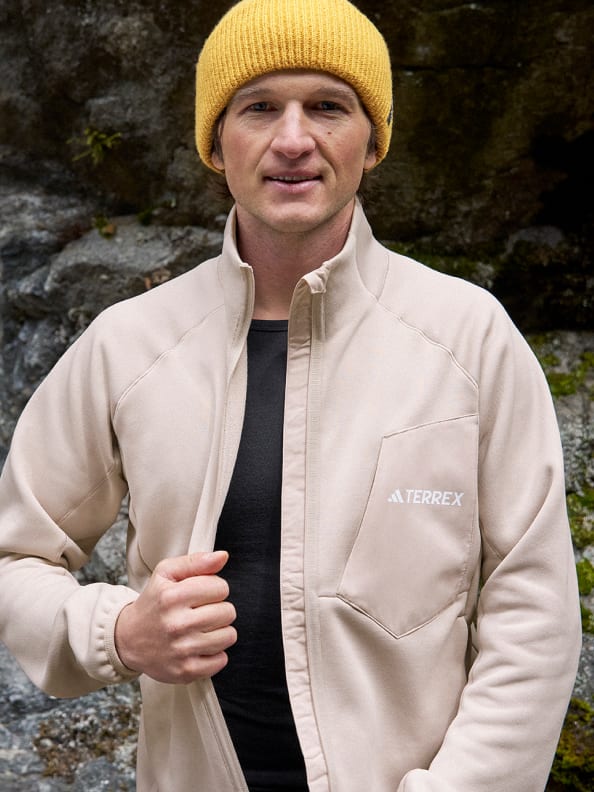Man unzips the Terrex Xperior Medium fleece, revealing a black Xperior Merino base layer top, in front of a rock backdrop.