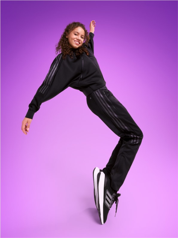 Smiling young girl standing on her toes in adidas tracksuit.