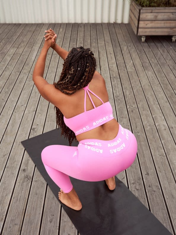 A woman wearing a pink bra and tights performs a deep squat as she trains indoors.