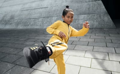 A model doing a karate kick wearing black shoes and yellow apparel from the adidas x LEGO® week collection.
