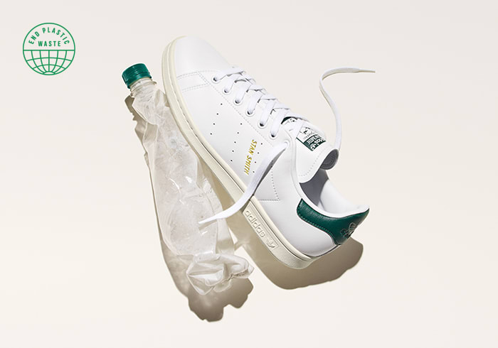 A Stan Smith shoe next to a crumpled water bottle on a white background.