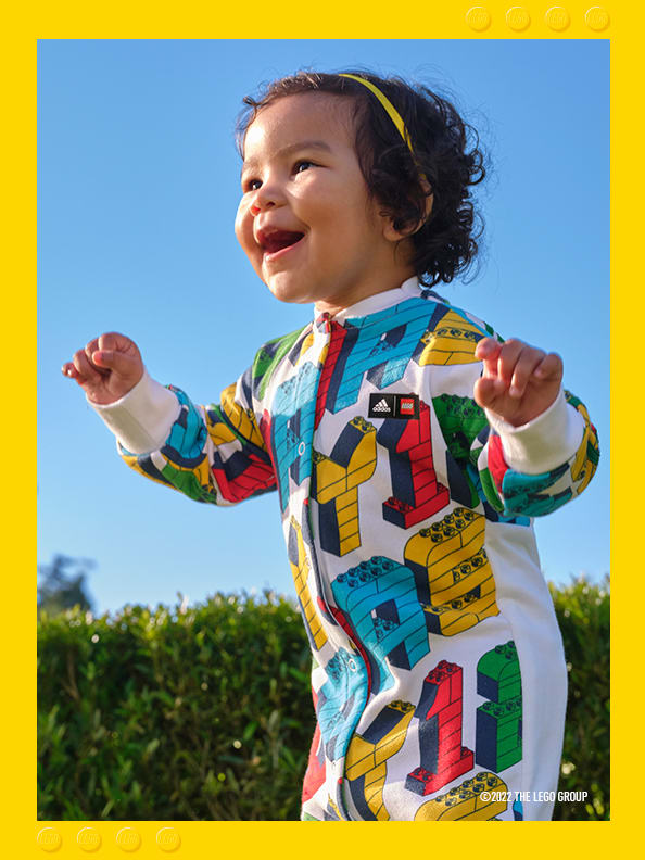 Infant girl smiling and playing in a park wearing a multicoloured adidas LEGO onesie