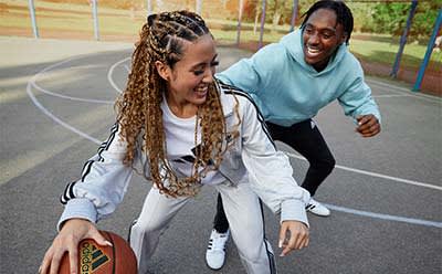 A male and female are playing basketball together on an outdoor basketball court.