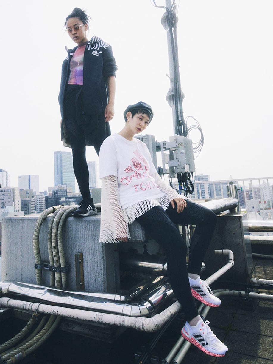 Two young women wearing items from HIROKO TAKAHASHI COLLECTION are standing on the rooftop overlooking Tokyo metropolis.